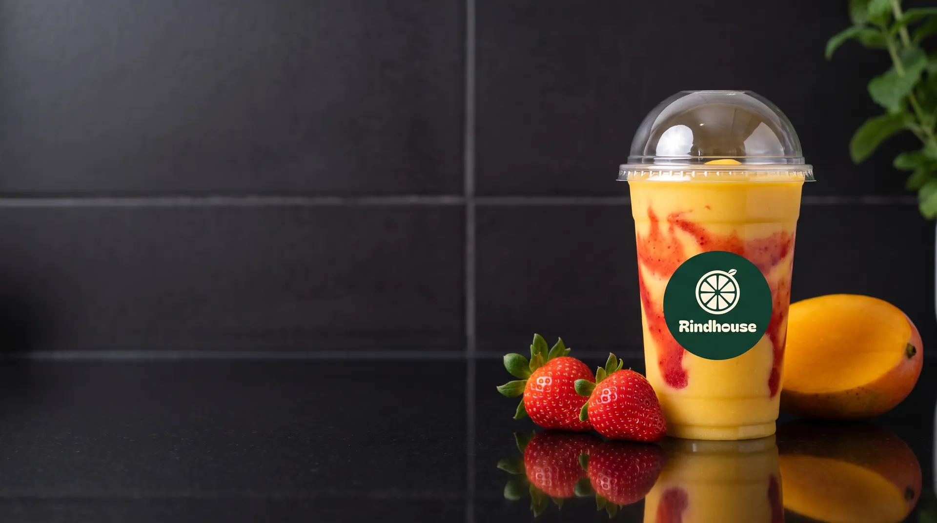 A mango smoothie on a Rindhouse counter, with halved oranges and limes beside it